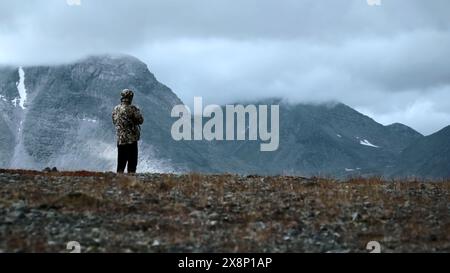 Uomo che fotografa il paesaggio montano altezza. Fermo. Vista posteriore di un uomo escursionista che scatta foto di pesanti nuvole e cime delle montagne. Foto Stock