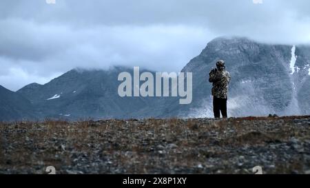 Uomo che fotografa il paesaggio montano altezza. Fermo. Vista posteriore di un uomo escursionista che scatta foto di pesanti nuvole e cime delle montagne. Foto Stock