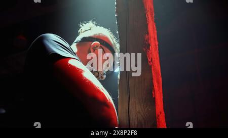 Vista ad angolo basso di un lavoratore che fissa una lanterna vintage su uno sfondo scuro. Supporto. Uomo che ripara l'antico lampione in legno. Foto Stock