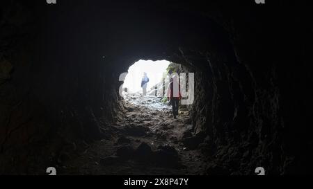Vista dalla grotta ai turisti. Fermo. Vista posteriore dell'uomo che esce dalla grotta. Il turista esce dalla grotta e diventa luce Foto Stock
