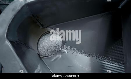 Versare una pila di particelle di plastica. Creatività. Processo di riempimento dei contenitori e pulizia delle particelle di plastica. Impianto per la lavorazione di granuli chimici di Foto Stock