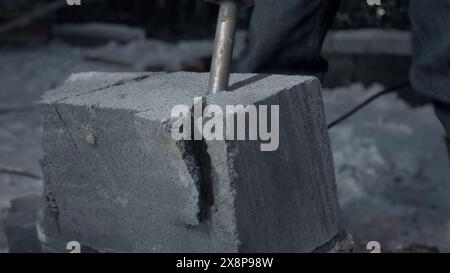 Man perfora blocchi di cemento. Fermo. Il lavoratore divide i blocchi di cemento nel cantiere con un martello perforatore. Rottura dei blocchi di cemento con un trapano Foto Stock