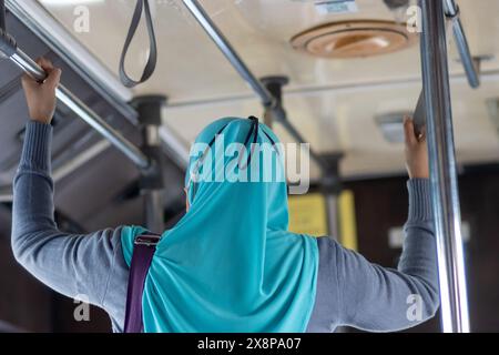 Una donna in piedi in tradizionale abito islamico tiene entrambe le mani durante il viaggio in autobus Foto Stock