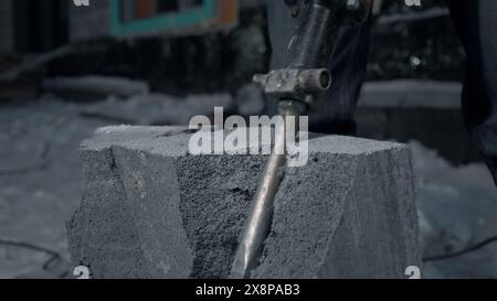 Man perfora blocchi di cemento. Fermo. Il lavoratore divide i blocchi di cemento nel cantiere con un martello perforatore. Rottura dei blocchi di cemento con un trapano Foto Stock