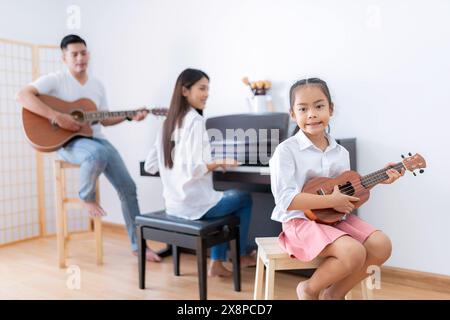 La famiglia si unisce a suonare musica. Padre suona la chitarra, madre suona il pianoforte. Figlia che gioca a ukulele Foto Stock