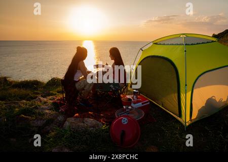 Due escursioniste si accamparono su una scogliera sul mare. Le escursioniste bevono un caffè mentre si godono il tramonto. Foto Stock