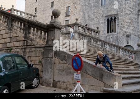 Un ragazzo si arrampica dalla banister di pietra di una grande scalinata a girona, la gente sale le scale, con edifici storici in pietra sullo sfondo. Foto Stock