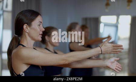 Gruppo di persone sportive durante un allenamento in palestra con un allenatore. Supporto. Gruppo di ragazze di atleti che oscillano le mani prima di iniziare una sessione di yoga di allenamento. Foto Stock