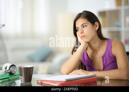 Studente apatico che guarda lontano seduto nel soggiorno di casa Foto Stock