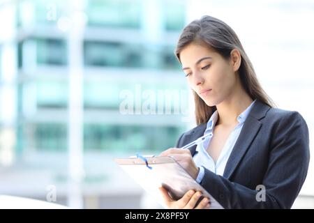 Un dirigente serio che compila il modulo in piedi per strada Foto Stock