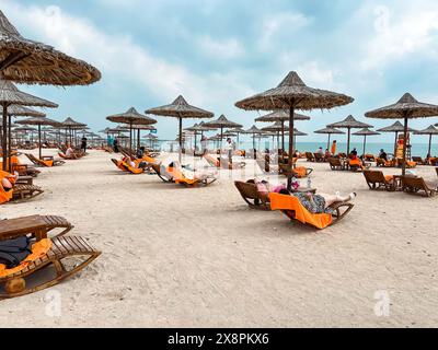 Sir Bani Yas, Emirati Arabi Uniti - 5 gennaio 2024: I visitatori si rilassano sui lettini sotto gli ombrelloni di paglia su una tranquilla spiaggia nell'isola di Sir Bani Yas. Foto Stock