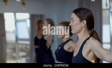 Gruppo di persone sportive durante un allenamento in palestra con un allenatore. Supporto. Gruppo di ragazze di atleti che oscillano le mani prima di iniziare una sessione di yoga di allenamento. Foto Stock