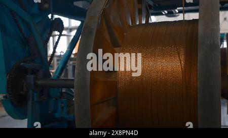 Bobine rotanti con fili metallici in fabbrica. Creatività. Avvolgimento di fibre metalliche su bobine presso l'impianto metallurgico. Processo di torsione nelle bobine di Foto Stock
