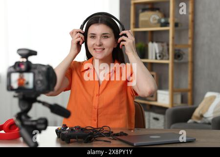 Blogger con tecnologia sorridente che indossa le cuffie mentre registra video a casa Foto Stock