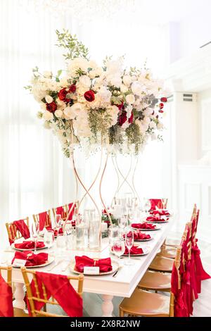 Tavolo per ricevimenti nuziali con alti centrotavoli floreali e decorazioni rosse Foto Stock