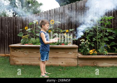 bambino di 6 anni in pantaloncini corti e infradito che tiene in mano uno sparkler nel cortile Foto Stock