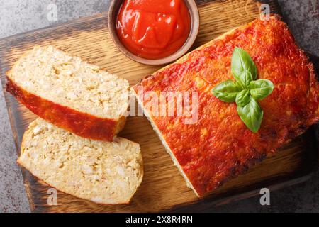 Polpettone con tritatutto di pollo, cipolla e aglio glassati con ketchup primo piano sul bordo di legno sul tavolo. Vista dall'alto orizzontale Foto Stock