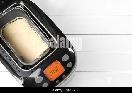 Macchina per il pane con impasto crudo su un tavolo di legno bianco, vista dall'alto. Spazio per il testo Foto Stock