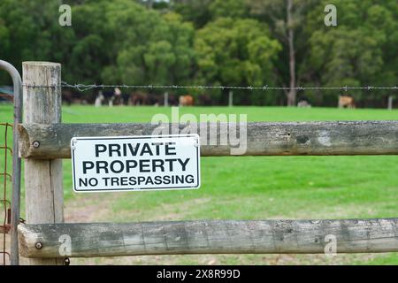 Un cartello indicante la proprietà privata No Trespassing sulla recinzione di legno di un allevamento di bovini con un paddock verde e bestiame sullo sfondo. Foto Stock