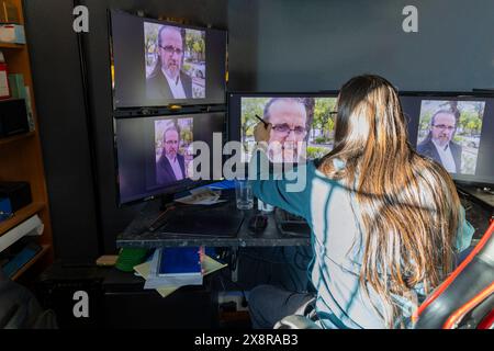 un uomo si siede davanti a diversi monitor di computer ritoccando un'immagine di se stesso. Ha i capelli lunghi, la barba e indossa gli occhiali. Foto Stock