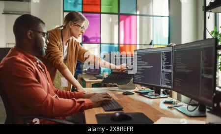 L'ingegnere del software afroamericano mostra il codice sul computer desktop a Project Manager femminile in Stylish Office. Uomo nero e donna caucasica discutono dei progressi nello sviluppo di applicazioni ai. Foto Stock