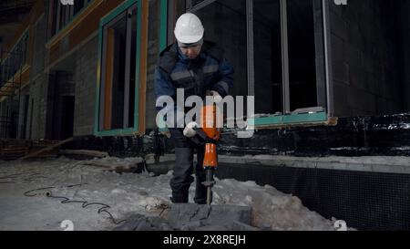 Man perfora blocchi di cemento. Fermo. Il lavoratore divide i blocchi di cemento nel cantiere con un martello perforatore. Rottura dei blocchi di cemento con un trapano Foto Stock