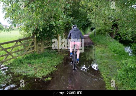 Eton Wick, Windsor, Regno Unito. 27 maggio 2024. Un ciclista attraversa le acque alluvionali vicino a Roundmoor Ditch nel villaggio di Eton Wick, Windsor, Berkshire. Crediti: Maureen McLean/Alamy Live News Foto Stock