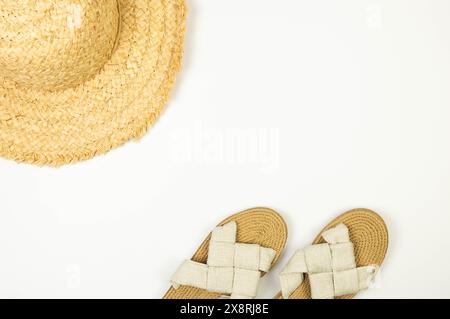 Vista dall'alto del cappello di paglia e delle pantofole su sfondo bianco. Moda estiva, vacanze e carta da parati da spiaggia. Copia spazio, disposizione piatta. Foto Stock