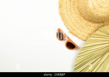 Vista dall'alto di cappello di paglia, foglie di palma essiccate e occhiali da sole su sfondo bianco. Moda estiva, vacanze e carta da parati da spiaggia. Copia spazio, disposizione piatta. Foto Stock