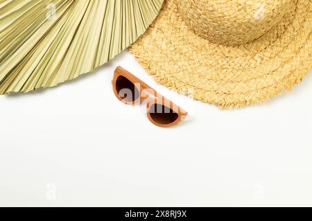 Vista dall'alto di cappello di paglia, foglie di palma essiccate e occhiali da sole su sfondo bianco. Moda estiva, vacanze e carta da parati da spiaggia. Copia spazio, disposizione piatta. Foto Stock