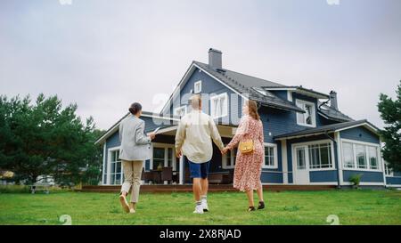 Agente immobiliare che mostra una bella grande casa a una giovane coppia di successo. Persone in piedi fuori in un caldo giorno su un prato, parlare con una donna d'affari, discutere di comprare una nuova casa. Foto Stock