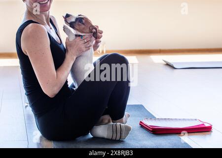 Ragazza felice che fa yoga con un cucciolo Jack Russell terrier in camera con una finestra aperta. Stile di vita sano e meditazione Foto Stock