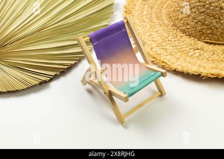 Sedia da spiaggia colorata, cappello di paglia, foglie di palma essiccate su sfondo bianco. Estate, vacanze e spiaggia. Composizione creativa, spazio di copia. Foto Stock