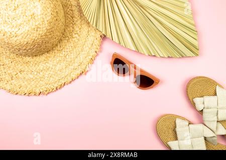 Vista dall'alto di cappello di paglia, foglie di palma essiccate, pantofole e occhiali da sole su sfondo rosa. Moda estiva, vacanze e carta da parati da spiaggia. Copia spazio, disposizione piatta. Foto Stock