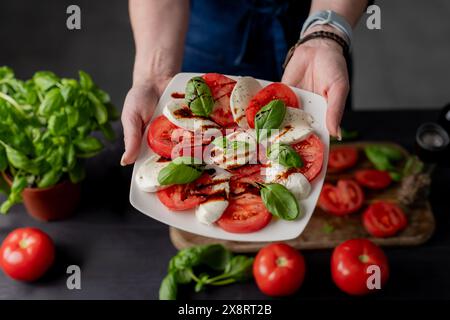 La donna tiene l'insalata caprese sul piatto, primi piani di pomodori e mozzarella Foto Stock