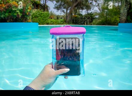 Concetto di donna influencer realizza video e foto dentro e sott'acqua con uno smartphone che si trova all'interno di una borsa impermeabile. Mano che tiene lo smartphone. Foto Stock