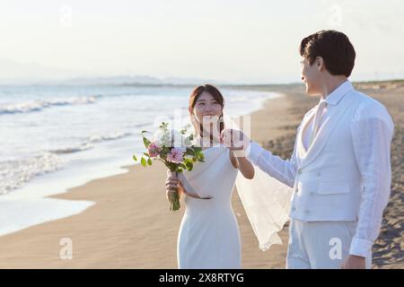 Sposa e sposo giapponesi che camminano sulla spiaggia Foto Stock