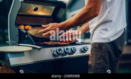 Uomo da vicino che prepara una bistecca di carne grigliata su un fuoco grill. Young Man Grilling Food for Outdoors Barbecue Dinner for Family. Foto Stock