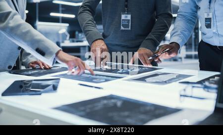 Responsabili anonimi in piedi intorno a un tavolo, in una riunione di lavoro, in cui discutono i progetti con la progettazione di apparecchiature industriali. Tecnici in piedi intorno al tavolo in ufficio. Primo piano sulle mani. Foto Stock