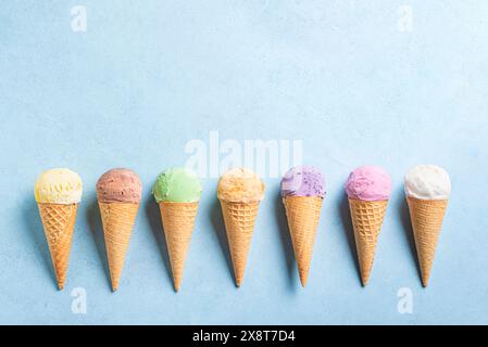 Varie palline da gelato in coni su sfondo blu, vista dall'alto, spazio per copiare. Set di gelato colorato in coni per waffle. Foto Stock