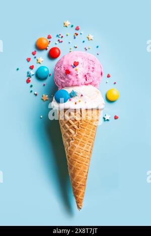 Una tazza di gelato alla vaniglia e alle fragole in un cono di cialda decorato con spolverini di zucchero su sfondo blu. Disposizione creativa e alla moda delle sessole da gelato. Foto Stock