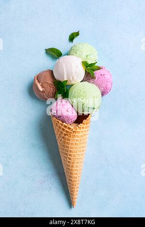 Cono per gelato con vari cucchiai su sfondo blu, piatto e creativo. Molti gelati biologici colorati nel cono per waffle. Foto Stock