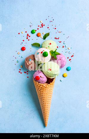 Cono per gelato con vari cucchiai e spolverini di zucchero luminosi su sfondo blu, layout estivo creativo. Molti gelati biologici colorati in W Foto Stock