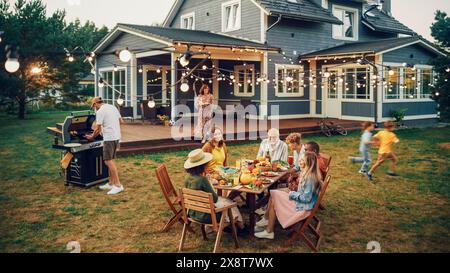 Grande famiglia e amici che festeggiano fuori a casa. Gruppi diversi di bambini, adulti e anziani si sono riuniti a un tavolo e hanno avuto conversazioni divertenti. Preparare barbecue e mangiare verdure. Foto Stock