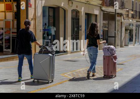 Due donne viste con la schiena irriconoscibile camminare con le proprie valigie su una strada pedonale Foto Stock