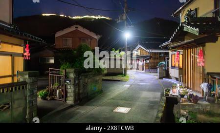Case tradizionali su strada vuota a Takeda di notte con un castello illuminato sulla collina Foto Stock