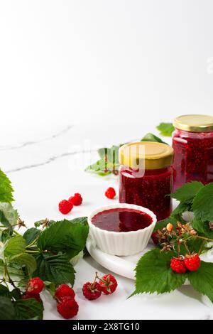 Conservazione estiva fatta in casa, marmellata di lamponi in vasetti, vasetti con marmellata e ciuffi di lamponi Foto Stock