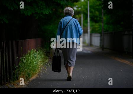 Una donna anziana con una borsa della spesa viene vista camminare in un parco di Varsavia, Polonia, il 23 maggio 2024. Foto Stock