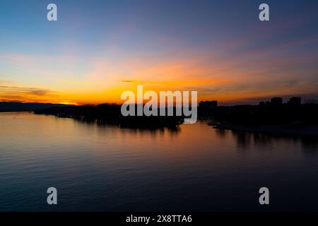 Lo splendido tramonto illumina il fiume Danubio a Novi Sad, Serbia, con vivaci sfumature di arancione e blu, che si riflettono pacificamente sulle acque calme Foto Stock