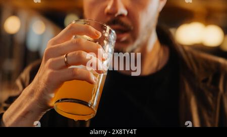 Primo piano Ritratto di un bel giovane uomo sposato caucasico che beve gustose bevande rinfrescanti Golden Beer in un pub. Gli appassionati di calcio si godranno una bevanda fredda prima dell'inizio della trasmissione di eventi sportivi dal vivo. Foto Stock